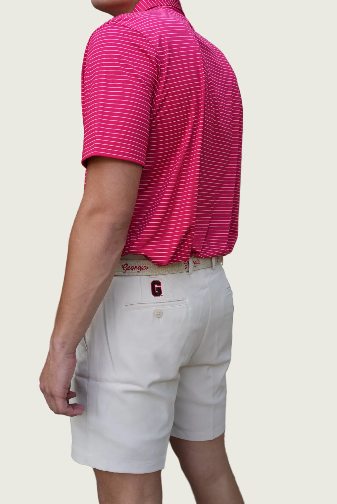 A man wearing a bright pink and red striped polo shirt and off-white chino shorts, shown from the back in an outdoor residential setting.