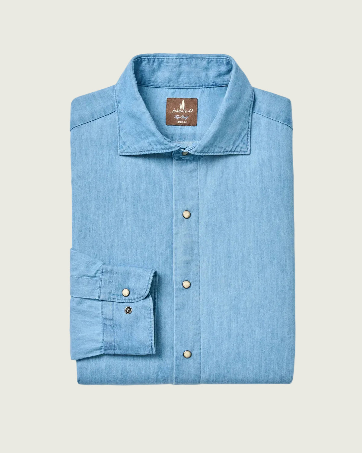 A folded light blue chambray button-down shirt with a pointed collar and a single cuff, displayed on a clean white background. The brand label inside the collar reads 'Majestic'.