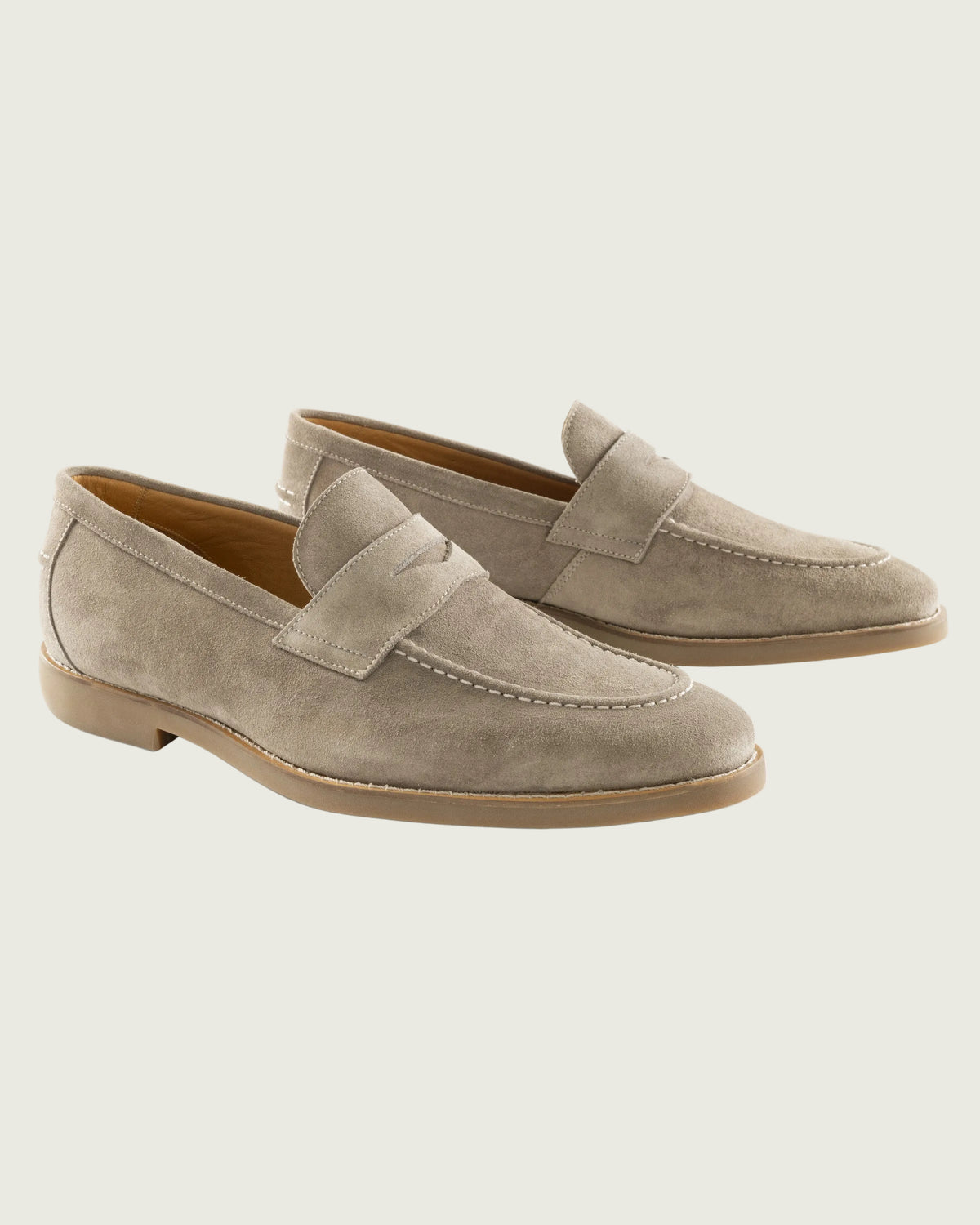 A pair of taupe suede penny loafers with contrast stitching and low stacked heels, displayed on a clean white background.