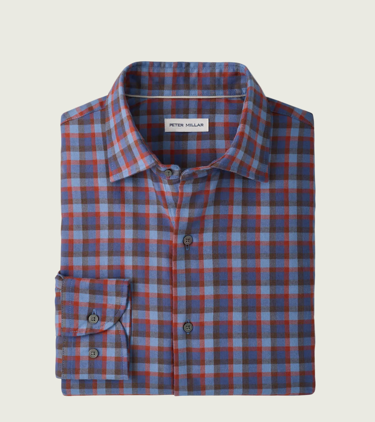 A folded long-sleeve button-up shirt by Peter Millar, featuring a blue, red, and gray plaid pattern, displayed on a clean white background.