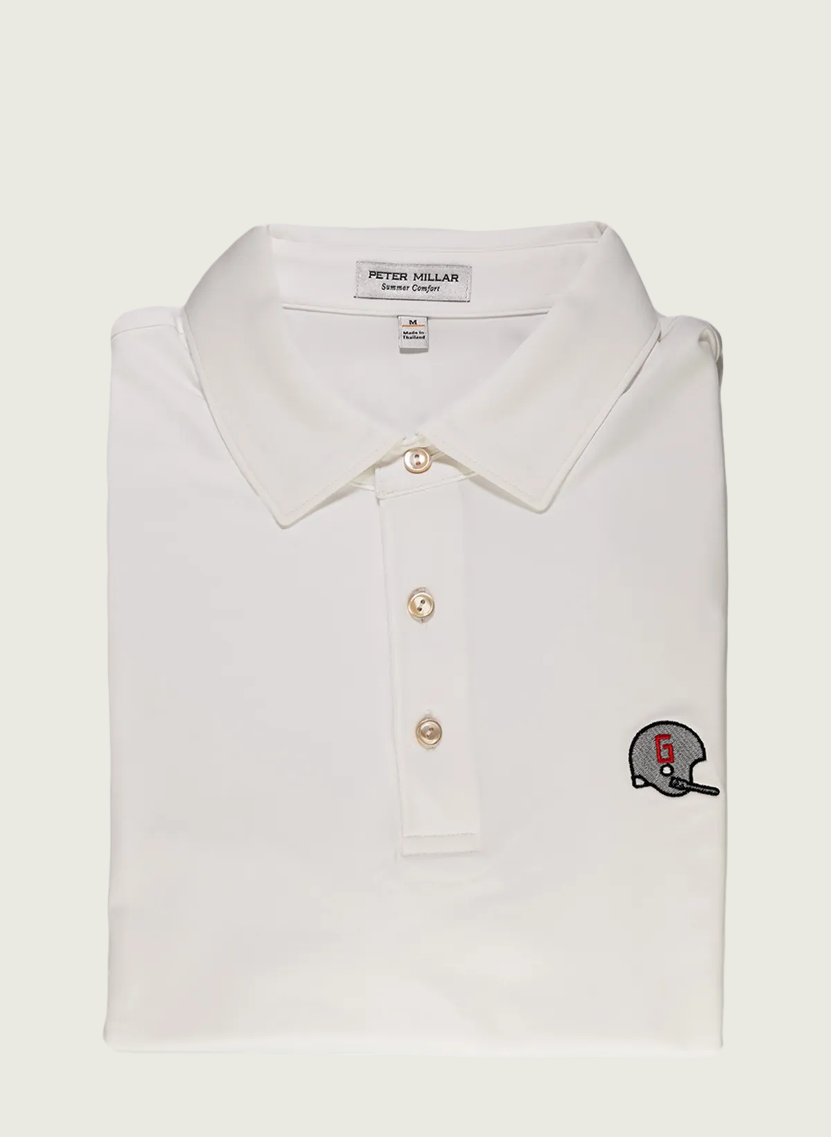 A white Peter Millar solid stretch jersey polo shirt with a vintage UGA football helmet embroidery on the chest.