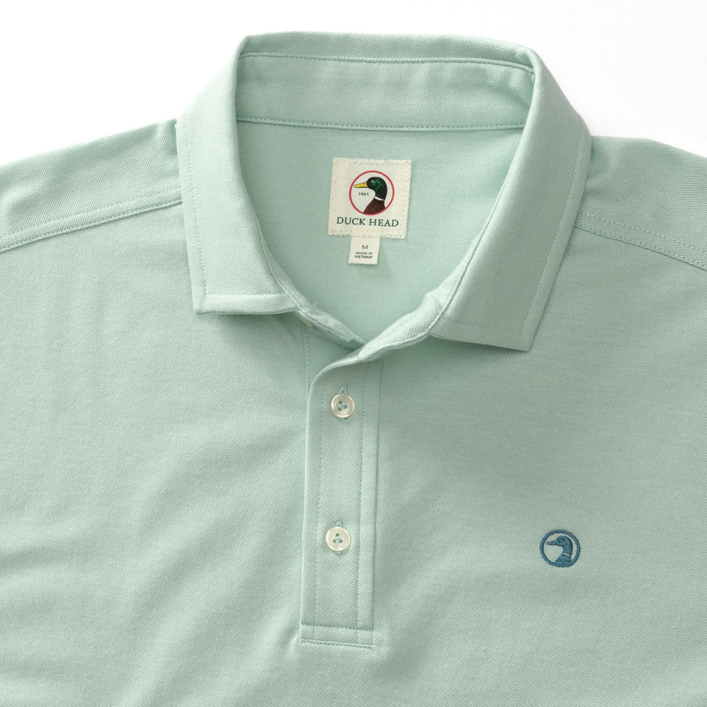 Close up of pique polo shirt with three off white buttons in color Surf Spray, similar to a seafoam green.