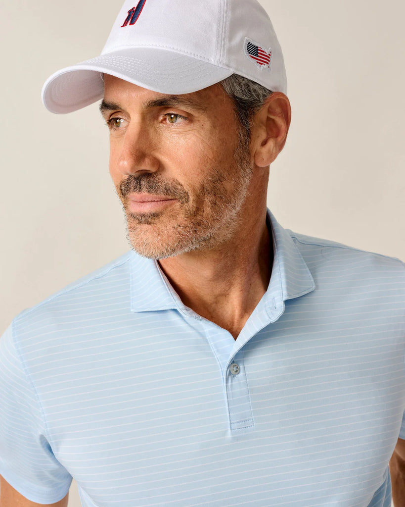 Man wearing a light blue striped polo shirt and white cap with logos on a beige background