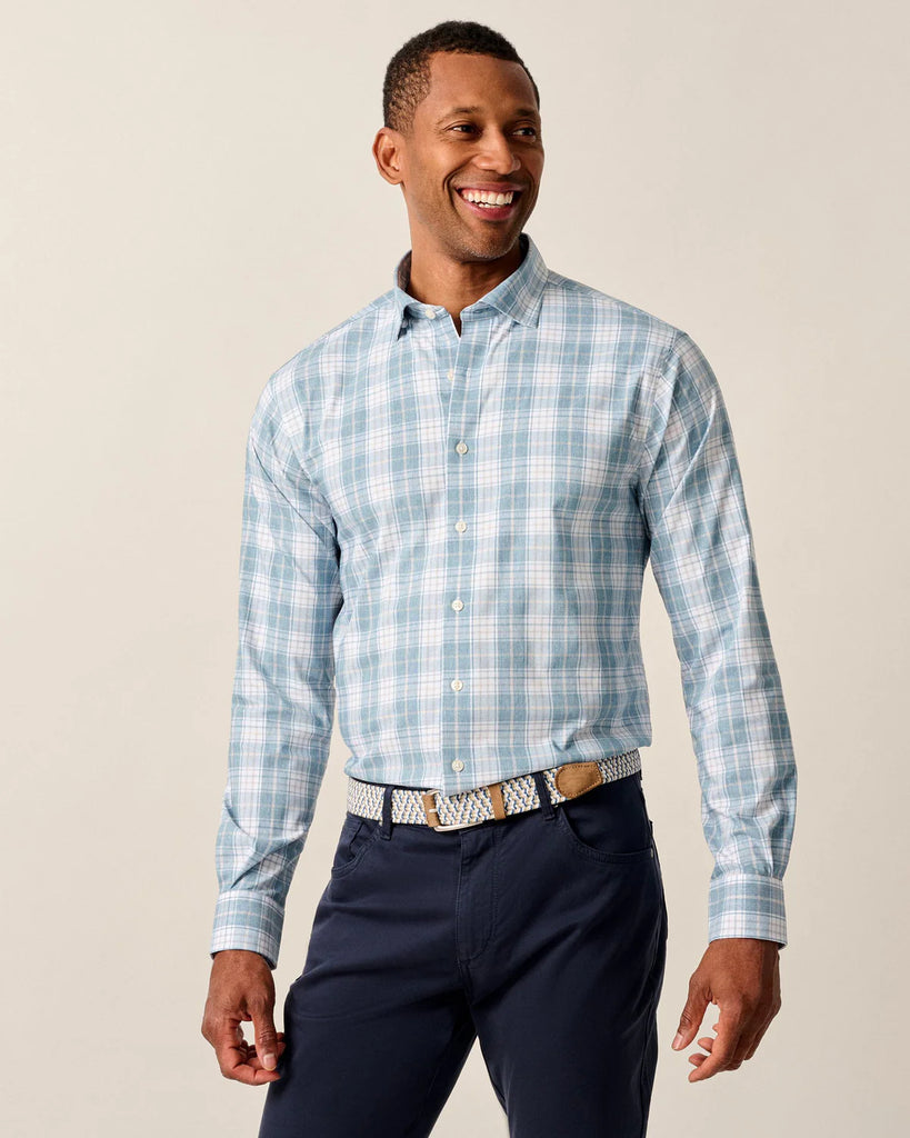 Man wearing a blue plaid shirt and navy pants against a beige background