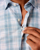 Close-up of a person buttoning a light blue plaid shirt.