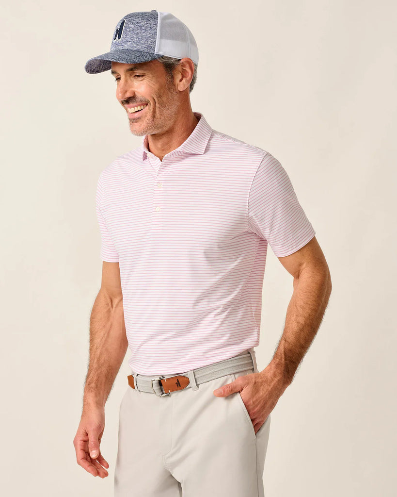 Man wearing a pink striped polo shirt, light gray cap, and beige pants on a plain background
