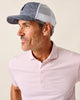 Man wearing a gray and white cap and a pink striped polo shirt against a beige background