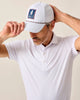 Man wearing a white cap with a logo and a white patterned shirt against a beige background