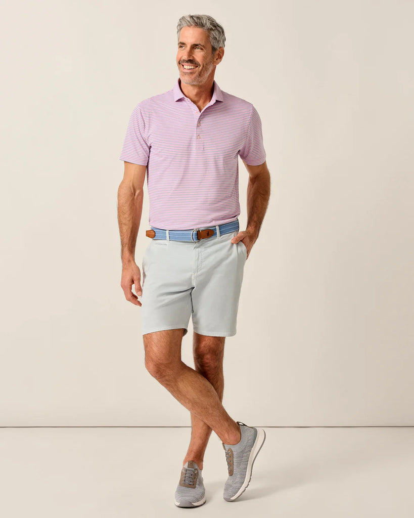 Man wearing a pink and blue striped polo shirt and light blue shorts against a beige background