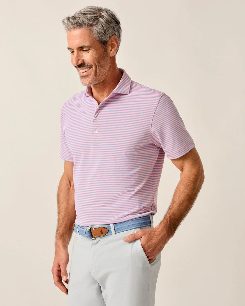 Man wearing a pink and blue striped polo shirt and light blue pants against a beige background