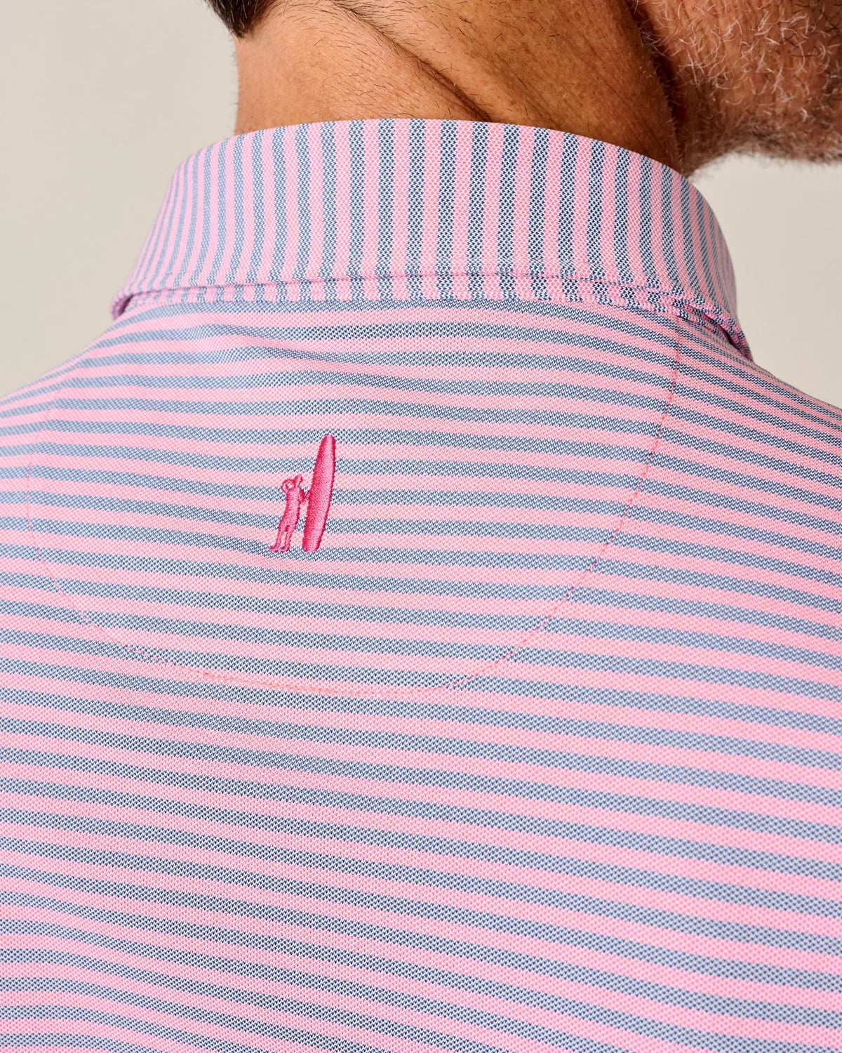 Pink and blue striped shirt with Johnnie-O logo on the nape of the neck against a neutral background