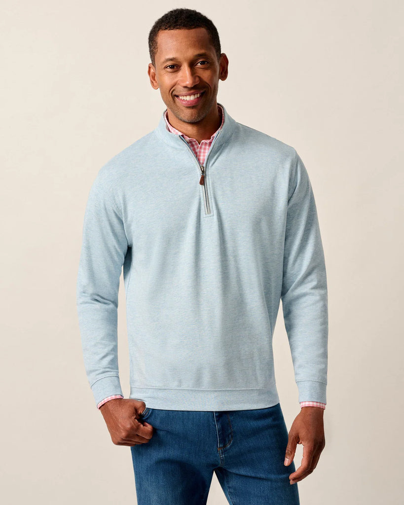 Man wearing a light blue quarter-zip sweater and blue jeans against a beige background