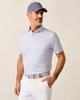 Man wearing a light purple patterned polo shirt, white pants, and a blue cap against a beige background