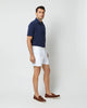 Side view shot of model wearing white shorts, brown leather loafers, and navy cotton terry polo shirt with white buttons.