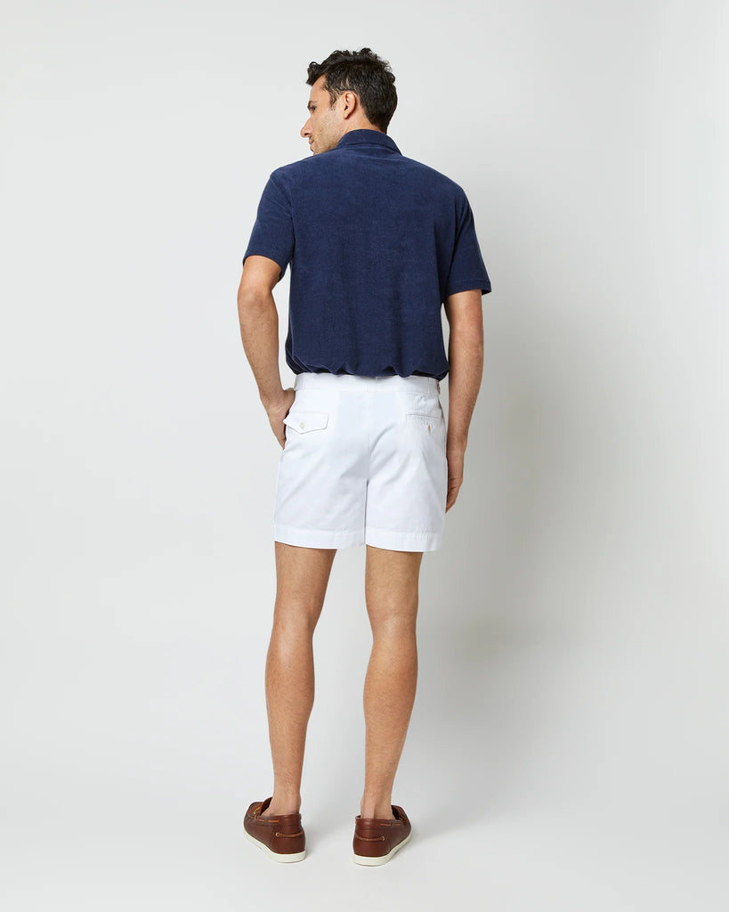 Back view shot of model wearing white shorts, brown leather loafers, and navy cotton terry polo shirt with white buttons.